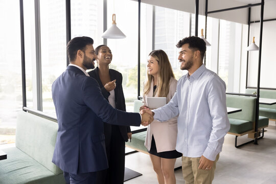Four multinational teammates, business partners met in modern co-working office shaking hands, greeting each other, express friendly relations and respect, start or finish briefing, negotiations event