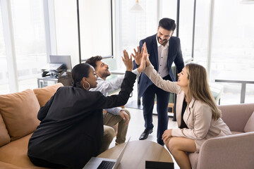 Four multinational teammates gathered together in modern coworking space giving high five, gesture...