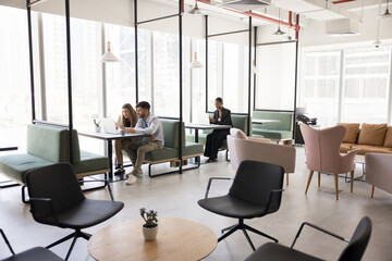 People engaged in collaboration and individual work in productive atmosphere, two colleagues working on laptop, freelancer woman make remote job seated at table in modern, open-space coworking area