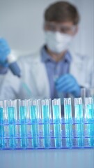 Test tubes with a blue liquid, close-up view. Scientist holding pipette conducting experiments in...