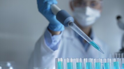 Woman scientist researcher using a micropipette to fill up test tubes with a blue liquid in...