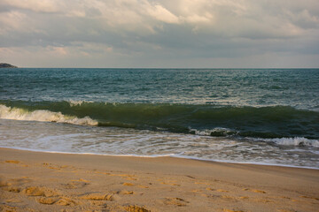 Scenic beach view with gentle ocean waves crashing onto the sandy shore. The turquoise sea stretches to the horizon under a partly cloudy sky, creating a tranquil and relaxing atmosphere.