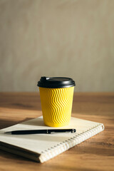 Paper cup and notepad with pen on wooden table, copy space.