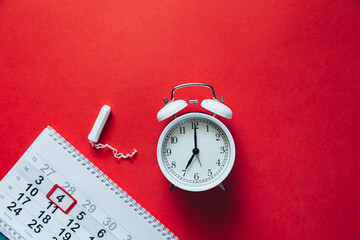 Menstruation, means of protection. Tampon and alarm clock on a red background.