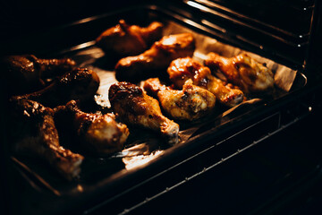 Baking tray with prepared chicken, baking chicken legs with sauce in oven.