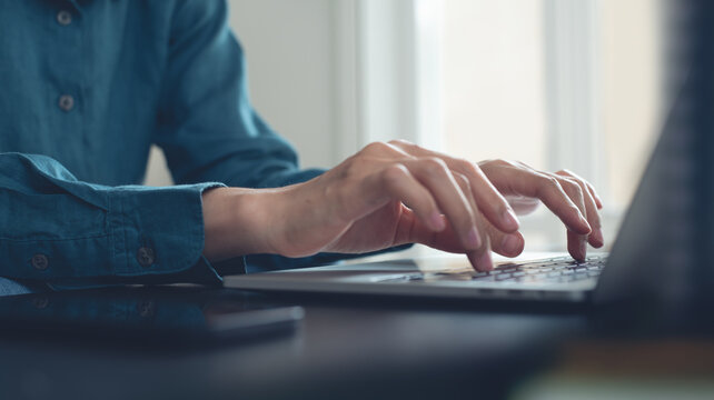 Business woman hand typing on laptop computer, surfing the internet, searching the information, online working at office with smart mobile phone, on table, side view, closeup, business technology