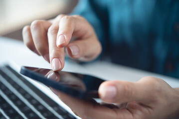 Closeup, woman using mobile phone with laptop computer on office table. Business woman surfing the internet, using smartphone, working on laptop computer at office