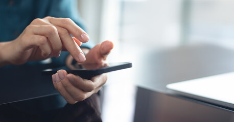 Woman using mobile phone with laptop computer on office table. Business woman surfing the internet, searching the information on smartphone working on laptop computer at workplace