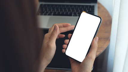 Mockup, Woman using mobile phone with blank white screen while online working on laptop at coffee shop. Business woman using smartphone, mockup for online marketing, mobile app, closeup