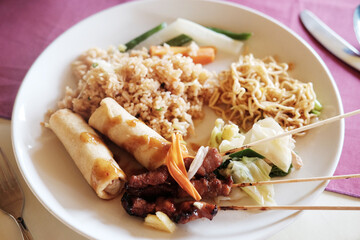 Close up BBQ food or barbecue grilled chicken with fried rice and spring rolls on white dish is tradition food in Bali, Indonesia
