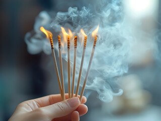 A hand is holding several burning incense sticks with smoke