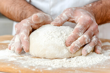 Hands shaping a ball of dough on a wooden surface, covered in flour