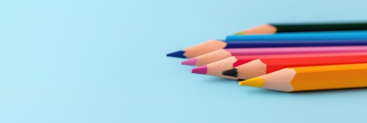 Fototapeta premium A row of pencils with different colors are lined up on a blue background. The pencils are arranged in a way that they are all pointing in the same direction, creating a sense of unity and order