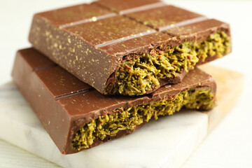Pieces of tasty Dubai chocolate with pistachios and knafeh on white wooden table, closeup