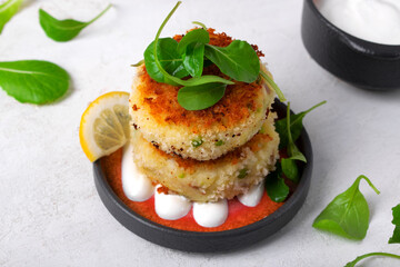 Two cutlets of pollock, potatoes, green peas and cheese, served with lemon-sour cream sauce on a plate, garnished with spinach