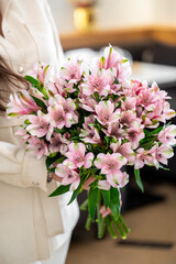 A close-up of a person holding a vibrant bouquet of pink alstroemeria flowers. The delicate petals and lush greens stand out against a softly blurred background, symbolizing beauty and elegance.