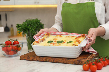Woman putting baking dish with tasty spinach lasagna onto white marble table indoors, closeup