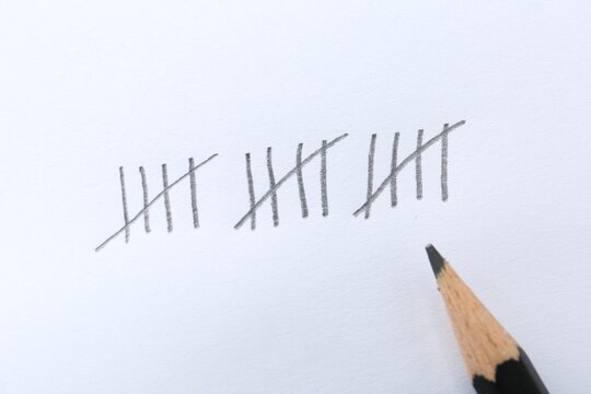 Counting days by drawing sticks with pencil on white background, closeup