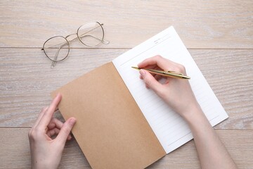 Woman writing in copybook at wooden table, top view