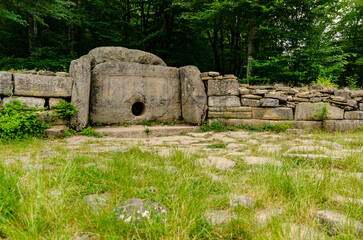 Dolmen set amidst dense forest, surrounded by lush greenery. Stone structure features central hole,...