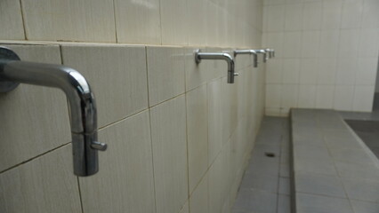 Row of stainless steel faucets on tiled wall