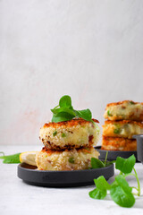 Stack of white fish fillet cutlets, potatoes, green peas and cheese garnished with spinach on grey plate on white table