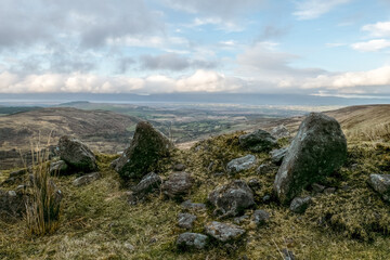 High vantage point. Collection of dark rocks on a grassy slope. View of a sprawling valley below.