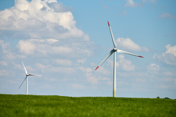 Wind turbine stands tall in lush green wheat field beneath bright blue sky with fluffy white clouds...