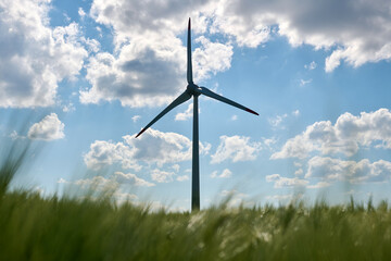 Single wind turbine silhouetted against bright blue sky with scattered fluffy clouds and blurred...