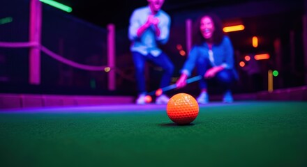 Young adults enjoying neon lit mini golf game with orange ball on green course