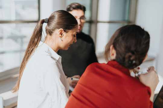 A group of business employees engage in a casual discussion in a bright office kitchen setting. The image conveys teamwork, collaboration, and a relaxed work environment.