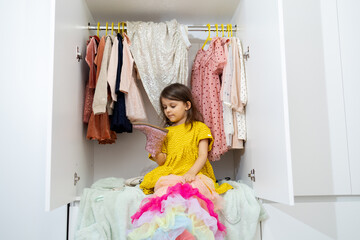 child near a wardrobe with dresses chooses dresses and having fun. The shopaholic concept