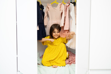 child near a wardrobe with dresses chooses dresses and having fun. The shopaholic concept