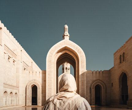 Person mit R&uuml;cken zur Kamera verh&uuml;llt vor imposanten Hintergrund der Sultan-Qabus-Gro&szlig;en-Moschee im Oman