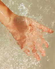 Fototapeta premium A hand reaches down to touch the calm, clear surface of the water. Sunlight creates ripples and reflections on the water. The image conveys a sense of tranquility.