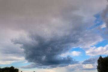 Blue sky with storm clouds over the deciduous tree tops