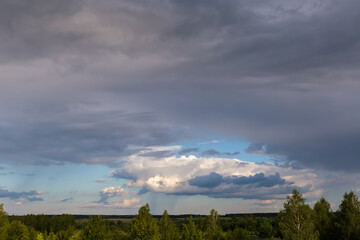 Blue sky with cumulus and storm clouds over the trees