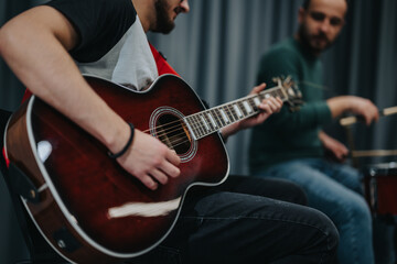 Obraz premium A group of musicians practicing with an acoustic guitar and drums, creating music together. The setting has a casual and creative atmosphere in a studio environment.