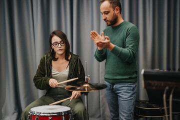 Two individuals collaborate in a music studio, focusing on drum playing and learning techniques.