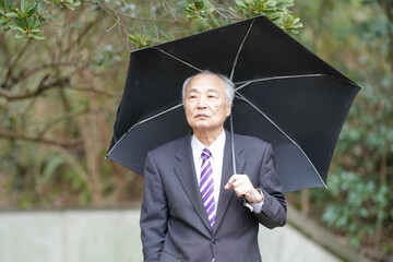A park on a rainy day in Japan with lots of greenery in spring. A Japanese man in his late 70s...