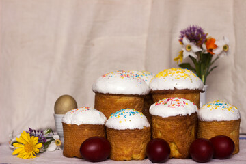 Easter bread with icing and colourful sprinkles on a table with Easter eggs and spring flowers. Place for text