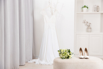 Beautiful wedding bouquet and bridal shoes on pouf indoors