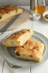 Pieces of delicious focaccia bread with olives, thyme, salt and knife on white wooden table, closeup