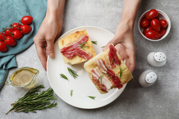 Woman serving delicious focaccia bread at grey table, top view