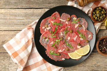 Delicious beef carpaccio with arugula, capers, cheese and lemon on wooden table, flat lay