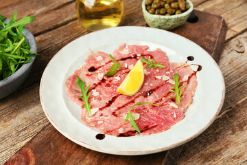 Delicious beef carpaccio with arugula, cheese, balsamic vinegar and lemon on wooden table, closeup