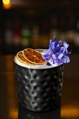 Exotic Cocktail in a Textured Metal Cup with Dried Lemon and Purple Flowers