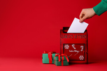 Man putting letter into Santa Claus mailbox against red background, closeup with space for text. Christmas tradition