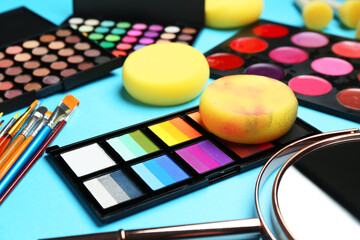 Bright face paints, brushes, mirror and sponges on light blue background, closeup