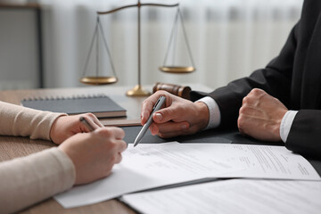 Notary pointing at document and client putting signature at table indoors, closeup